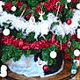 cat, christmas_tree, ornaments, red, white, green, garland, toy_train, floor, tile_floor, holiday_decor, festive, indoor, animal, pet, cozy, black_and_white_cat, christmas, decorations, tree_skirt
