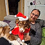 Enya a rejoint le concours — aidez-le/la à gagner de superbes lots ! man, dog, santa_hat, scarf, indoor, couch, smiling, glasses, home, radiator, door, wall, furniture, pet, brown_dog, white_paws, celebration, holiday, relaxed, happy