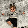Alaia is registered to the contest to win money with this photo: toddler, child, baby, girl, smiling, face, hair, pigtails, gray_sweater, black_pants, socks, blanket, soft_texture, indoor, floor, cute, relaxed, portrait, clothing, person