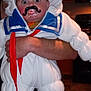 Rowan is registered to the contest to win money with this photo: baby, child, costume, pacifier, mustache, stay_puft_marshmallow_man, white, blue, red, kitchen, adult_hand, wide_eyes, expression, indoors, floor, cabinet, stove, person, funny, holding