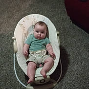 Rowan is registered to the contest to win money with this photo: baby, infant, rocker, carpet, couch, blanket, child, indoor, furniture, seat, person, clothing, shorts, green_shirt, floor, living_room, expression, head, legs, feet