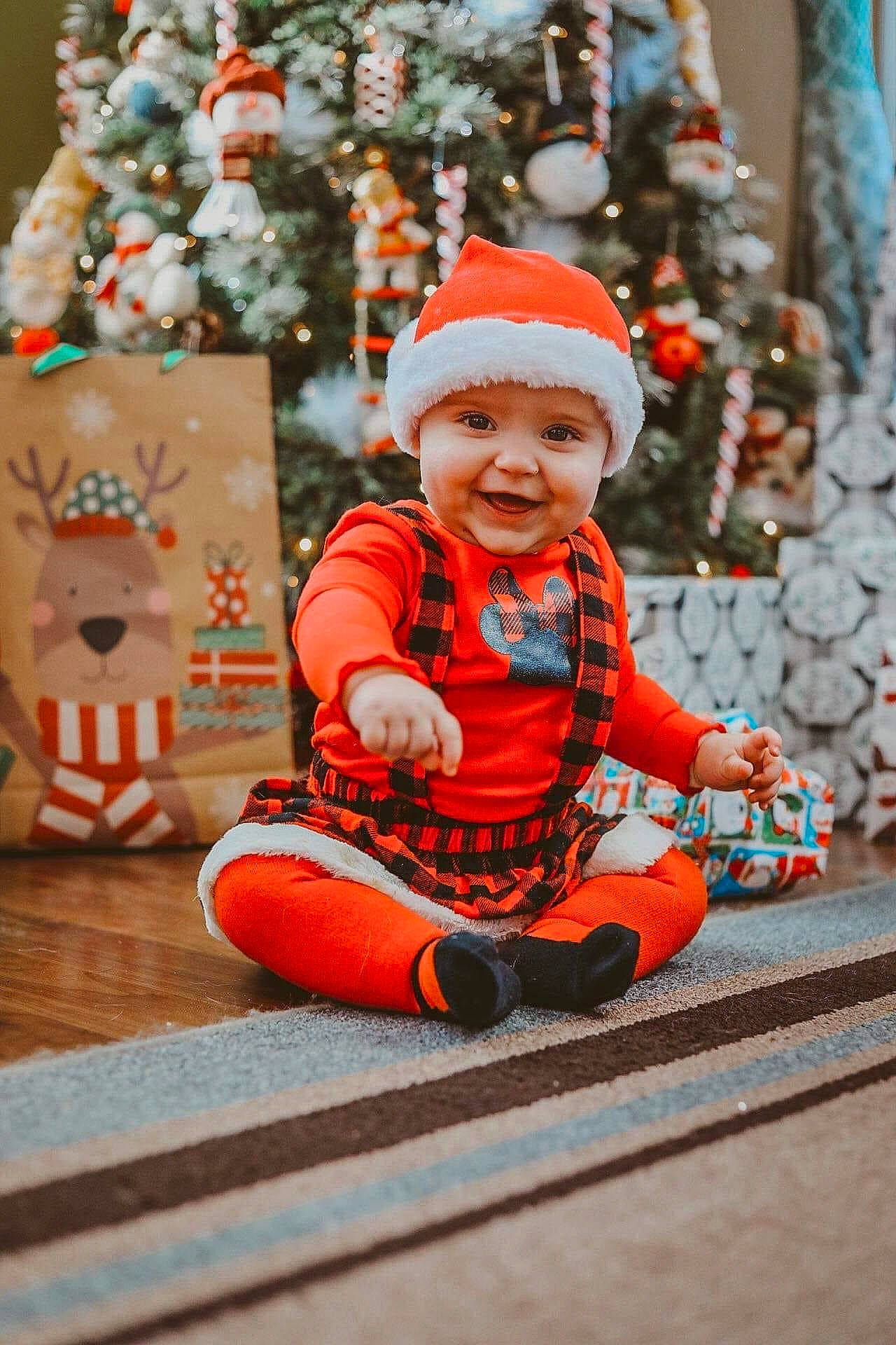 Adeline is registered to the contest to win money with this photo: baby, baby_toddler_clothing, child, christmas_decoration, christmas_ornament, christmas_tree, event, flooring, fun, happy, headwear, holiday, ornament, outerwear, person, plant, smile, standing, toddler, tree