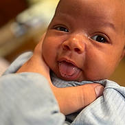 Ky is registered to the contest to win money with this photo: baby, infant, face, tongue, hand, skin, expression, closeup, cute, child, person, newborn, portrait, soft, blurred_background, clothing, blue, smile, playful, gentle