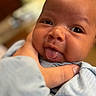 baby, infant, face, tongue, hand, skin, expression, closeup, cute, child, person, newborn, portrait, soft, blurred_background, clothing, blue, smile, playful, gentle