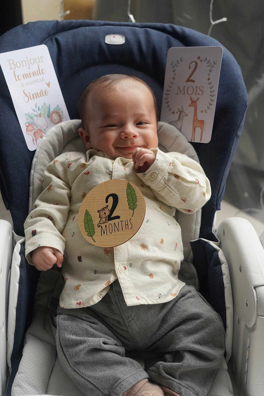 Simão a rejoint le concours — aidez-le/la à gagner de superbes lots ! baby, infant, smile, clothing, shirt, pants, baby_seat, milestone_card, text, hand, face, cute, child, indoor, comfort, happy, young, portrait, sitting, cozy