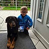 Orko participe au concours pour gagner de l'argent avec cette photo : boy, child, dog, pet, indoor, doorway, mat, glasses, blue_jacket, black_dog, tan_paws, tile_floor, greenery, outdoor, railing, window, curtain, side_door, casual, portrait