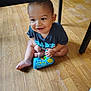 Zakarian is registered to the contest to win money with this photo: baby, child, smiling, toy, floor, wooden_floor, indoor, toddler, blue_shirt, sitting, happy, face, person, play, foot, table, cute, young_child, home, casual