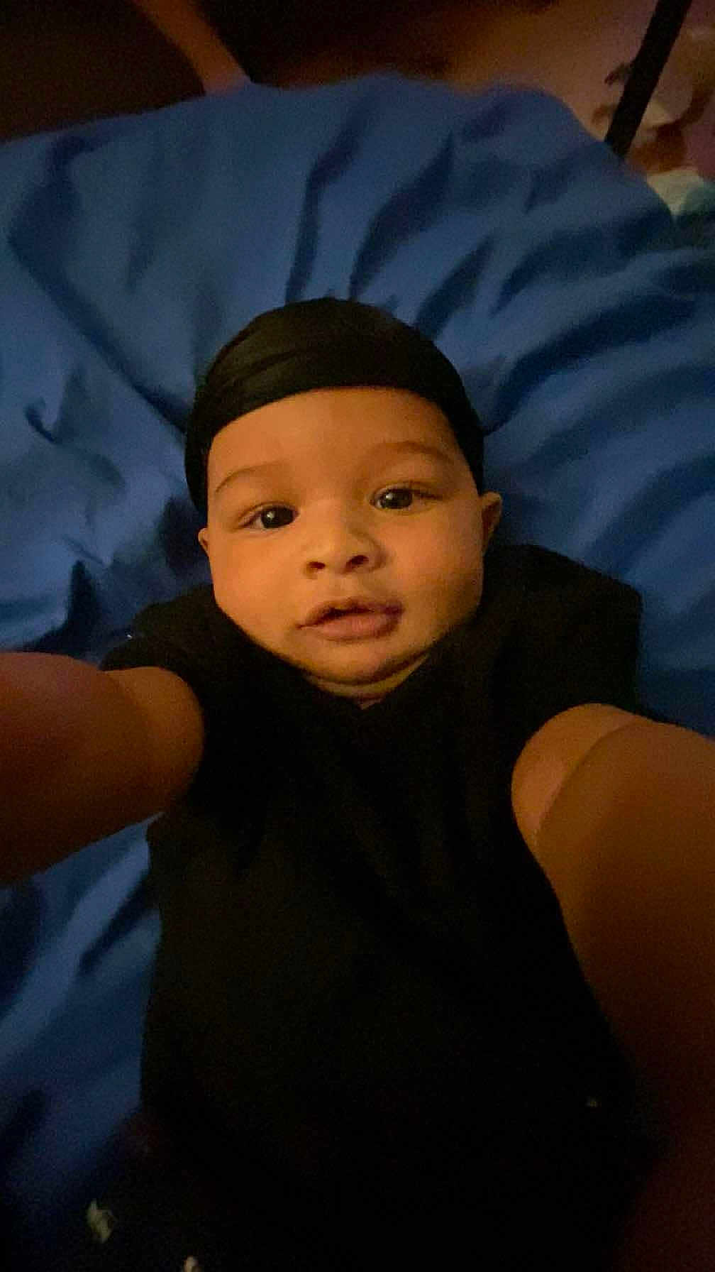 Zakarian is registered to the contest to win money with this photo: baby, child, selfie, black_clothing, head_wrap, blue_blanket, indoor, cute, portrait, person, face, infant, lying_down, young_child, baby_girl, baby_boy, expression, looking_at_camera, skin, arms