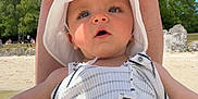 Kayden participe au concours pour gagner de l'argent avec cette photo : adult, baby, beach, blue_sky, child, curious, diaper, hat, infant, legs, nature, outdoor, protective, rocks, sand, striped_clothing, summer, sunny, trees, water