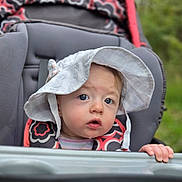 Iris joined the competition — help win amazing prizes! baby, child, infant, stroller, sun_hat, outdoor, portrait, face, eyes, wide_eyed, sitting, hand, gripping, floral_clothing, patterned_clothing, greenery, grass, daylight, closeup, adorable