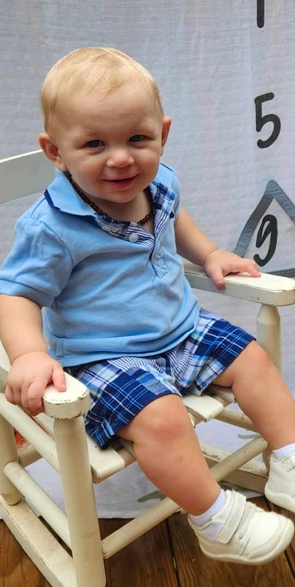 Huntley joined the competition — help win amazing prizes! toddler, child, smiling, blue_shirt, plaid_shorts, white_shoes, chair, wooden_chair, indoor, height_chart, happy, portrait, cute, baby, shorts, footwear, sitting, person, casual_clothing, light_hair