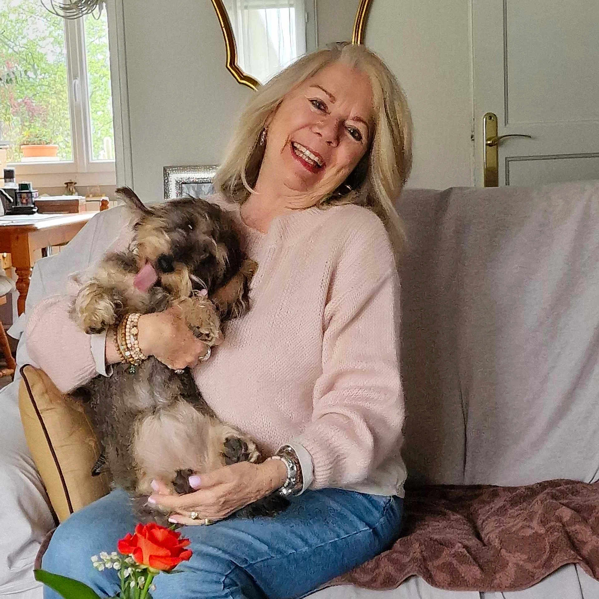 Truffe participe au concours pour gagner de l'argent avec cette photo : woman, dog, indoor, couch, smiling, pet, happy, casual, sweater, jeans, bracelet, flower, living_room, window, home, furniture, door, natural_light, relaxed, cute