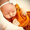 newborn, baby, sleeping, portrait, close_up, headband, flower, orange_clothing, knitwear, blanket, swaddled, infant, face, hands, peaceful, indoors, cozy, soft_lighting, candid, child