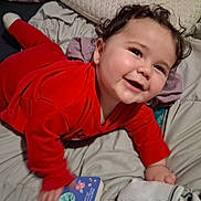 Johnathan joined the competition — help win amazing prizes! baby, child, smiling, red_clothing, bed, blanket, toy, book, happy, indoor, cute, face, hand, head, person, infant, cozy, lying_down, curly_hair, pajamas