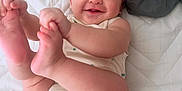 Liam is registered to the contest to win money with this photo: baby, infant, smiling, happy, cute, lying_down, bed, quilt, white, clothing, skin, hands, feet, face, person, child, one_person, indoor, infant_clothing, playful