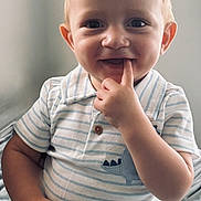 Cash is registered to the contest to win money with this photo: toddler, child, baby, smile, face, hand, finger, striped_shirt, dinosaur_patch, shorts, curly_hair, indoors, natural_light, portrait, cute, playful, sitting, happy, young_child, casual_clothing