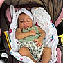 baby, infant, car_seat, blanket, headband, green_top, floral_clothing, sleepy, cute, infant_girl, child, resting, seat, soft_fabric, indoors, person, newborn, adorable, comfortable, peaceful