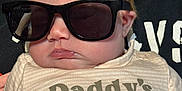 Allison is registered to the contest to win money with this photo: baby, child, sunglasses, face, person, clothing, infant, cute, portrait, young_child, toddler, shirt, text_on_clothing, casual, indoors, human, head, skin, expressionless, fashion
