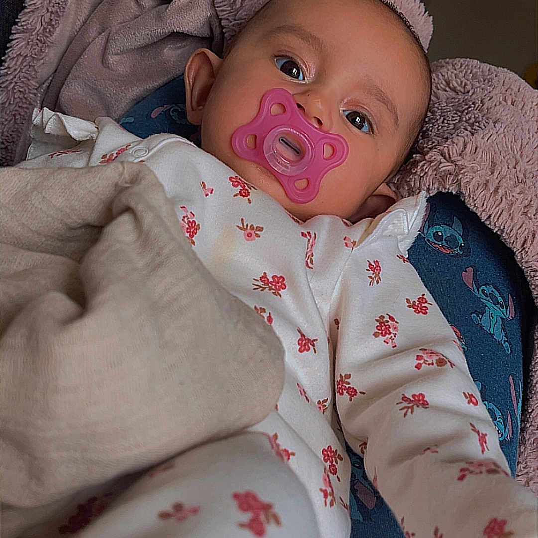 Ynaya participe au concours pour gagner de l'argent avec cette photo : baby, blanket, cartoon_pattern, child, comfort, cute, face, floral_pattern, head, indoors, infant, lying_down, pacifier, pajamas, person, plush, relaxing, room, sleepwear, soft_toy