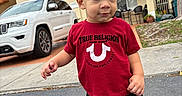 Kayden is registered to the contest to win money with this photo: black_shorts, blue_shoes, car, child, clothing, curious, daylight, house, outdoor, person, portrait, red_shirt, residential_area, sidewalk, street, suv, toddler, tree, urban, walking