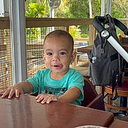 Kayden joined the competition — help win amazing prizes! casual, chair, child, daylight, expression, face, glass, greenery, hands, indoor, napkin, person, porch, smiling, stroller, table, toddler, turquoise_shirt, water, wooden_table