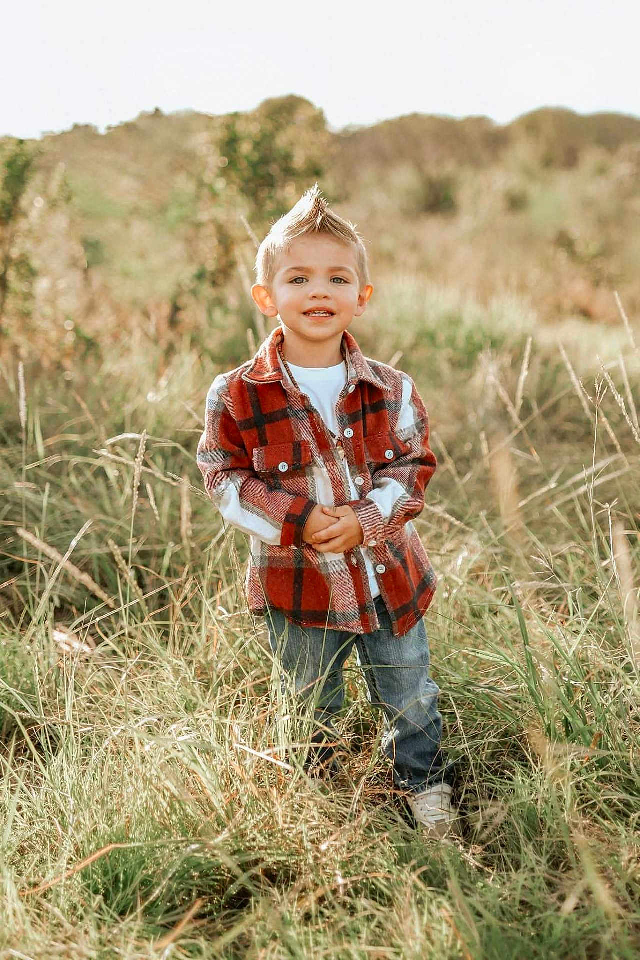 Juan Leo is registered to the contest to win money with this photo: child, boy, outdoor, grass, field, plaid_jacket, jeans, white_shirt, smiling, hairstyle, mohawk, casual_clothing, nature, sunlight, portrait, person, young, happy, standing, daytime