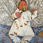 Oliver is registered to the contest to win money with this photo: newborn, baby, sleeping, onesie, pacifier, hat, animal_print, pillow, blanket, sports_theme, baseball, basketball, glove, infant, cute, resting, indoors, soft_lighting, child, peaceful