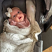 Aria joined the competition — help win amazing prizes! baby, infant, car_seat, blanket, bow, pink_clothing, face, headband, wrapped, cute, child, soft_texture, indoor, smiling, toddler, newborn, person, cozy, happy, closeup