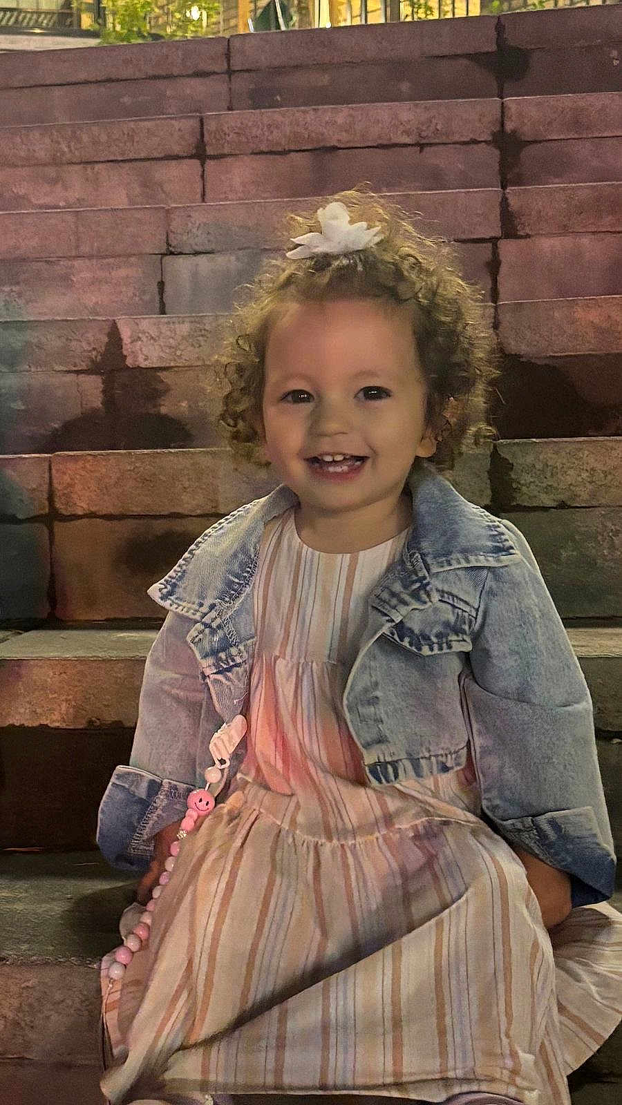 Kiana a rejoint le concours — aidez-le/la à gagner de superbes lots ! toddler, child, smiling, curly_hair, flower_hair_clip, denim_jacket, striped_dress, pacifier_clip, stairs, outdoor, night, happy, cute, person, portrait, sitting, young_child, clothing, fashion, accessory