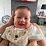 baby, smiling, infant, child, cute, happy, face, portrait, clothing, overalls, bear_design, person, indoor, living_room, furniture, hand, skin, head, short_hair, comfort
