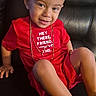 child, toddler, red_shirt, gold_chains, smile, leather_couch, sitting, casual, confident, indoor, short_hair, footwear, cute, portrait, young_child, positive_message, happy, fashion, person, relaxed