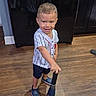 Izael is registered to the contest to win money with this photo: child, boy, baseball_bat, smiling, indoor, wooden_floor, shorts, jersey, footwear, crocs, cabinet, refrigerator, sportswear, playful, happy, person, standing, flooring, home, toy