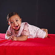 Daniel joined the competition — help win amazing prizes! baby, smiling, tummy, red_blanket, pink_clothing, happy, child, portrait, indoor, young_child, infant, cute, face, expression, lying_down, studio, dark_background, hands, short_hair, eyes