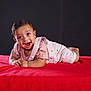 baby, smiling, tummy, red_blanket, pink_clothing, happy, child, portrait, indoor, young_child, infant, cute, face, expression, lying_down, studio, dark_background, hands, short_hair, eyes