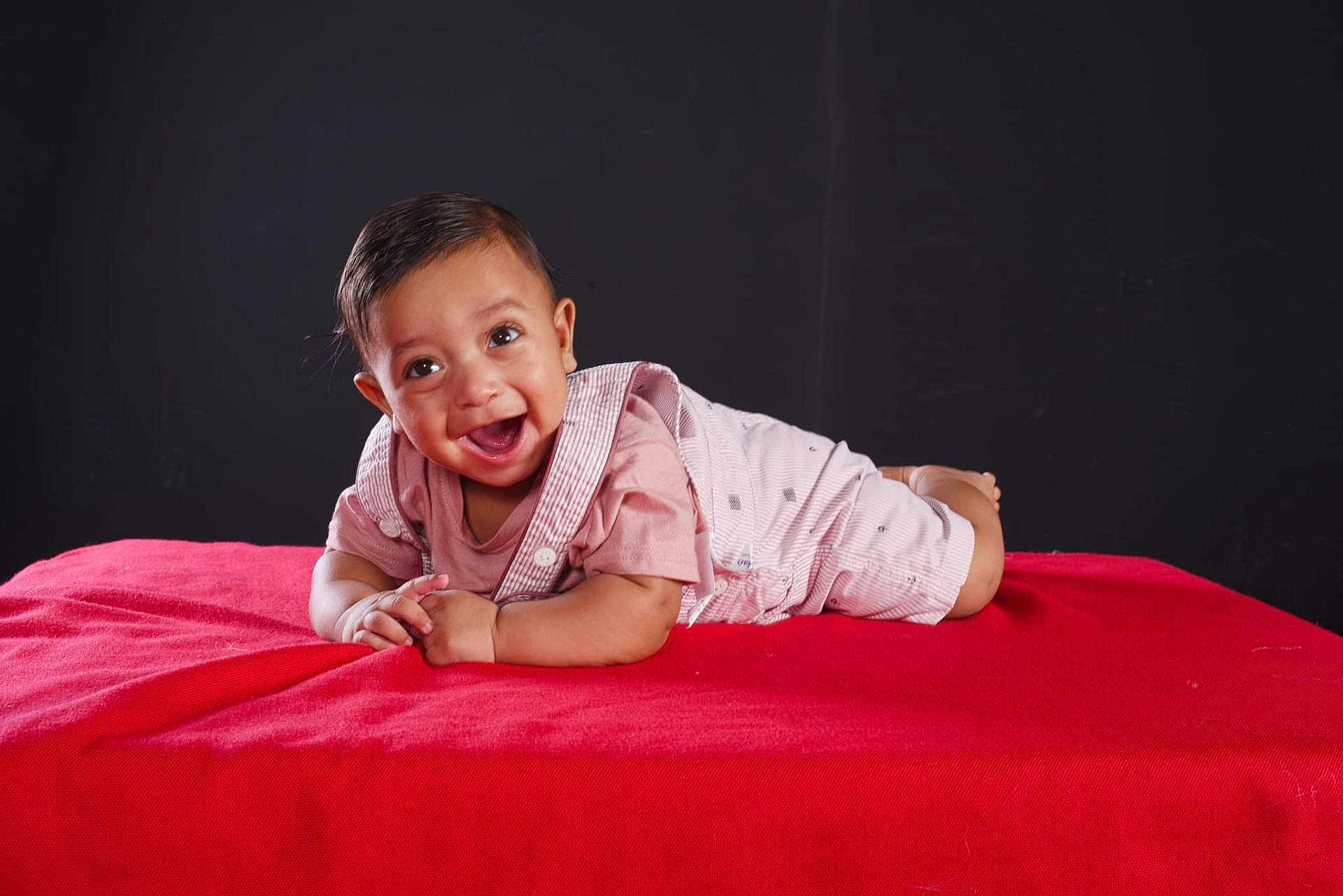 Daniel joined the competition — help win amazing prizes! baby, smiling, tummy, red_blanket, pink_clothing, happy, child, portrait, indoor, young_child, infant, cute, face, expression, lying_down, studio, dark_background, hands, short_hair, eyes