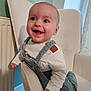 baby, chair, child, clothing, cute, expression, face, furniture, happy, head, indoor, infant, overalls, person, portrait, room, skin, smiling, white_shirt, window