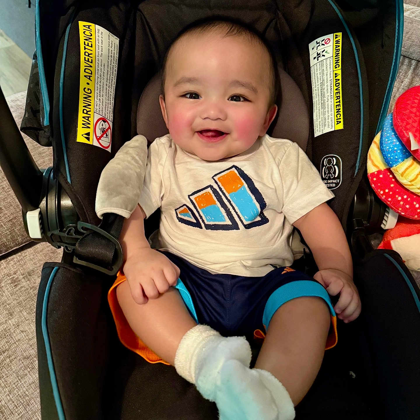 Ethan Mori is registered to the contest to win money with this photo: baby, car_seat, child, clothing, colorful, comfort, cozy, cute, face, happy, indoor, infant, person, rosy_cheeks, seat, shorts, smiling, socks, toy, tshirt