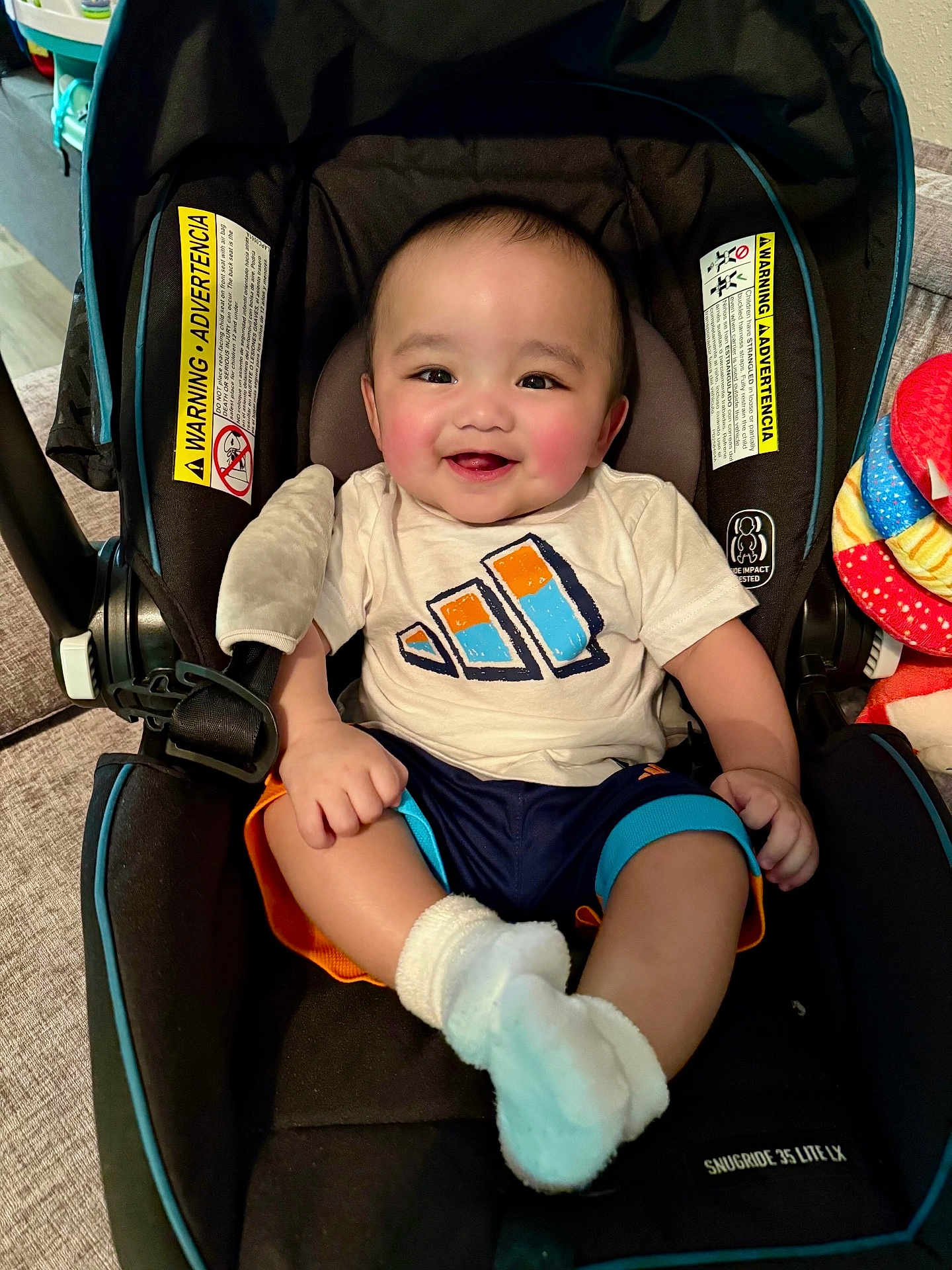 Ethan Mori is registered to the contest to win money with this photo: baby, smiling, car_seat, infant, child, happy, clothing, socks, indoor, person, face, cute, seat, comfort, rosy_cheeks, shorts, tshirt, toy, colorful, cozy