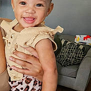 Naara joined the competition — help win amazing prizes! toddler, child, smile, headband, animal_print, clothing, person, indoor, living_room, couch, pillow, wooden_floor, wall, adult_hand, happy, fashion, cute, baby, portrait, holding