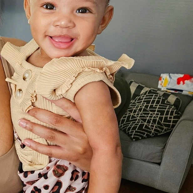 Naara joined the competition — help win amazing prizes! toddler, child, smile, headband, animal_print, clothing, person, indoor, living_room, couch, pillow, wooden_floor, wall, adult_hand, happy, fashion, cute, baby, portrait, holding