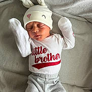 Lucas is registered to the contest to win money with this photo: baby, newborn, infant, hat, bunny_ears, clothing, shirt, pants, blanket, sleeping, cute, child, red_text, white_clothing, gray_pants, red_socks, soft_texture, portrait, lying_down, peaceful