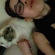 Princesse participe au concours pour gagner de l'argent avec cette photo : person, cat, glasses, indoor, lying_down, white_cat, gray_cat, face, pet, resting, closeup, casual, relaxed, dim_light, feline, companion, human, portrait, animal, cozy