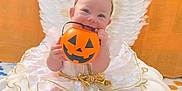 Stella joined the competition — help win amazing prizes! angel, baby, blanket, costume, cushion, cute, dress, festive, gold_bow, halloween, halo, holiday, infant, jack_o_lantern, orange_background, pumpkin_bucket, sitting, smiling, soft_texture, wings