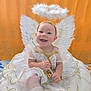 angel, baby, child, costume, cushion, cute, fabric, gold_trim, halo, happy, indoor, infant, orange_background, portrait, sitting, smiling, soft, wand, white_dress, wings
