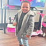 Zyon joined the competition — help win amazing prizes! child, toddler, smiling, portrait, standing, indoors, living_room, coat, jacket, jeans, boots, fashion, toy, scooter, television, cartoon, minnie_mouse, wooden_floor, happy, family_home