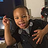 Zyon is registered to the contest to win money with this photo: child, toddler, smiling, grinning, portrait, indoors, seated, black_clothing, hand_gesture, short_hair, television, family_photos, living_room, furniture, chair, clothes, basket, blanket, home, photography