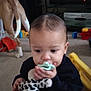toddler, child, pacifier, plush_toy, indoor, carpet, dog, toy, black_clothing, baby, person, floor, living_room, furniture, cute, young_child, animal, pet, playtime, home
