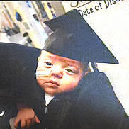 Dalton joined the competition — help win amazing prizes! baby, infant, graduation_cap, black_gown, nasal_tube, person, child, celebration, portrait, indoor, holding, face, headwear, medical, closeup, young_child, human, gown, event, candid