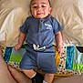 baby, child, smiling, blue_outfit, pillow, quilt, bed, feet, legs, black_shoes, white_socks, infant, happy, portrait, indoor, cute, person, fabric, text_on_clothing, relaxed
