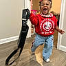 child, toddler, indoor, running, red_sweatshirt, hello_kitty, blue_pants, white_shoes, headband, black_strap, smiling, happy, curly_hair, wooden_floor, doorway, wall, person, clothing, playful, motion_blur
